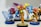 A collection of colorful figurines, with a focus on a central character in orange and yellow armor holding a blue weapon. Surrounding figures are similarly stylized with vibrant colors and dynamic poses, all standing on display bases.