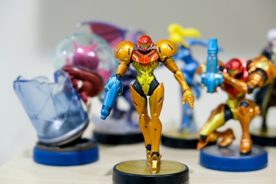 A collection of colorful figurines, with a focus on a central character in orange and yellow armor holding a blue weapon. Surrounding figures are similarly stylized with vibrant colors and dynamic poses, all standing on display bases.