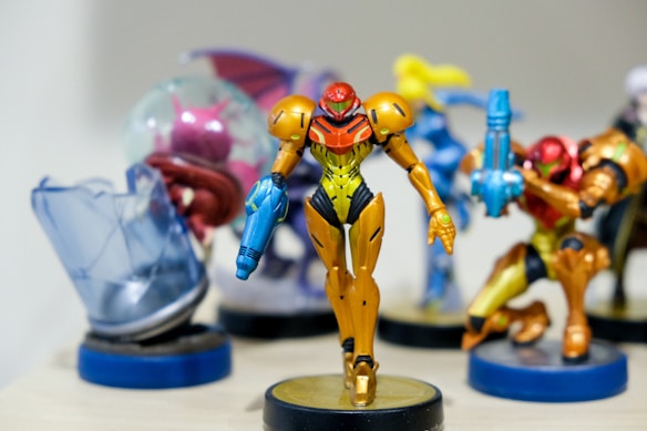A collection of colorful figurines, with a focus on a central character in orange and yellow armor holding a blue weapon. Surrounding figures are similarly stylized with vibrant colors and dynamic poses, all standing on display bases.