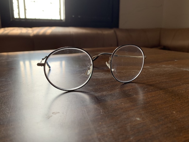 A close-up of stylish eyeglasses resting on a wooden table with soft natural light.