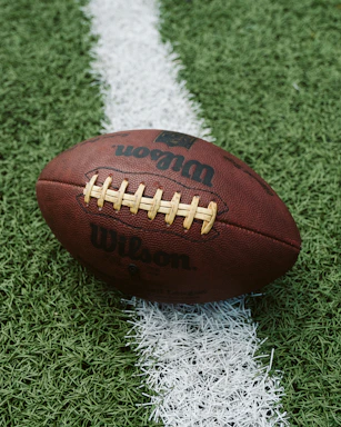 A close-up of a football on a vibrant green pitch under stadium lights.