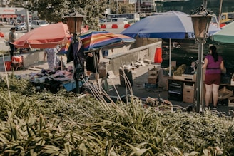 A bustling street scene in the rain, umbrellas bobbing past colorful market stalls