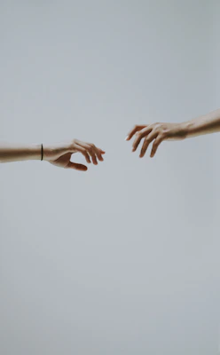 Two hands reaching toward each other against a plain light grey background