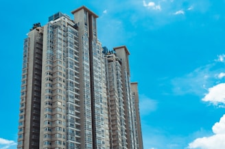 Tall residential skyscraper with modern architectural design, featuring large windows and multiple balconies, set against a bright blue sky.