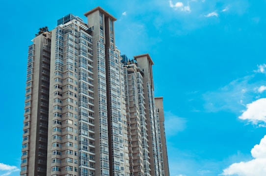 Tall residential skyscraper with modern architectural design, featuring large windows and multiple balconies, set against a bright blue sky.