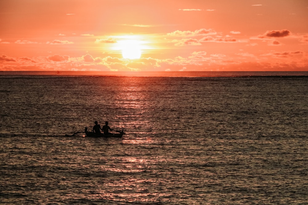 silhouette of two people near boat during sunset