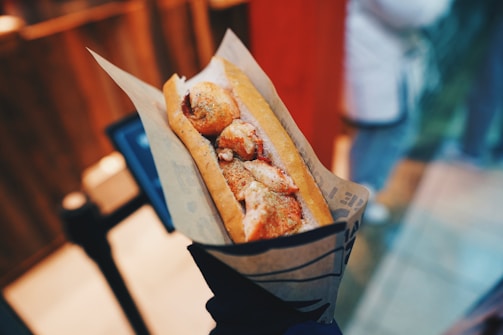Hands holding a hot dog in a jar with vibrant ingredients, highlighting the fresh and tasty appeal.