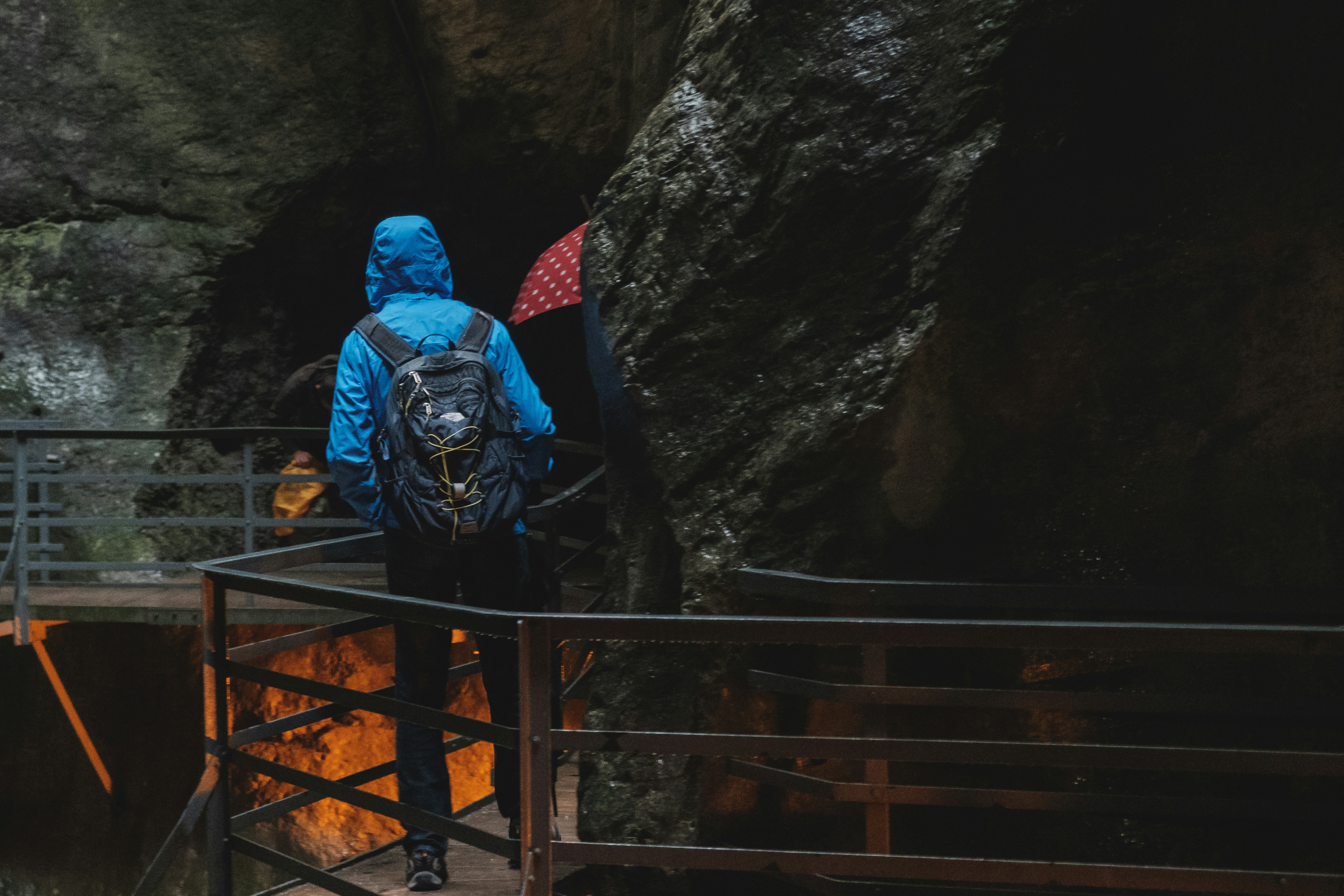 person wearing blue hooded jacket standing on footbridge near cave