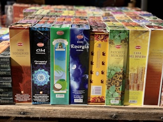 A variety of incense stick boxes are displayed in a row, featuring colorful and diverse designs. Each box has distinct branding and imagery, such as a blue Om design, coconut visuals, and vibrant patterns with gold accents.