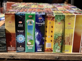 A variety of incense stick boxes are displayed in a row, featuring colorful and diverse designs. Each box has distinct branding and imagery, such as a blue Om design, coconut visuals, and vibrant patterns with gold accents.