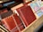 A collection of various leather-bound notebooks and journals, some featuring intricate stitching and embossed patterns. Next to them, there are maps folded into book-sized brochures. They are arranged in a wooden display.