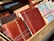 A collection of various leather-bound notebooks and journals, some featuring intricate stitching and embossed patterns. Next to them, there are maps folded into book-sized brochures. They are arranged in a wooden display.
