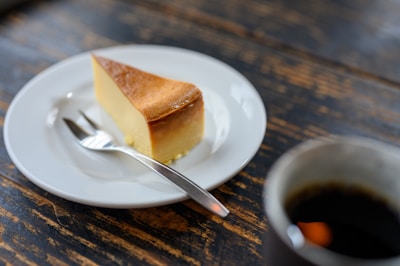 A steaming cup of coffee next to a slice of cheesecake on a rustic plate.