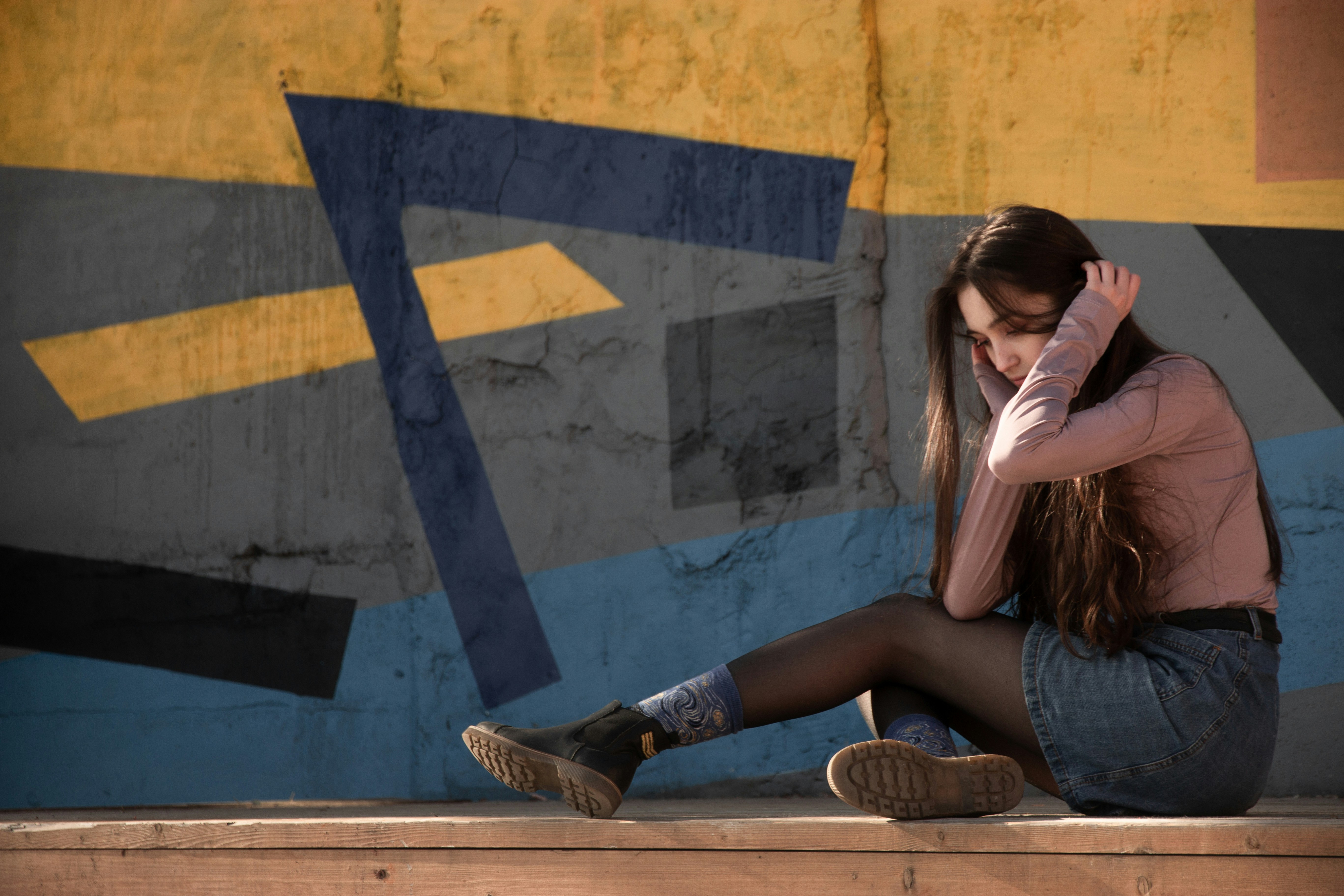 woman wearing gray long-sleeved shirt touching her head while sitting and looking down