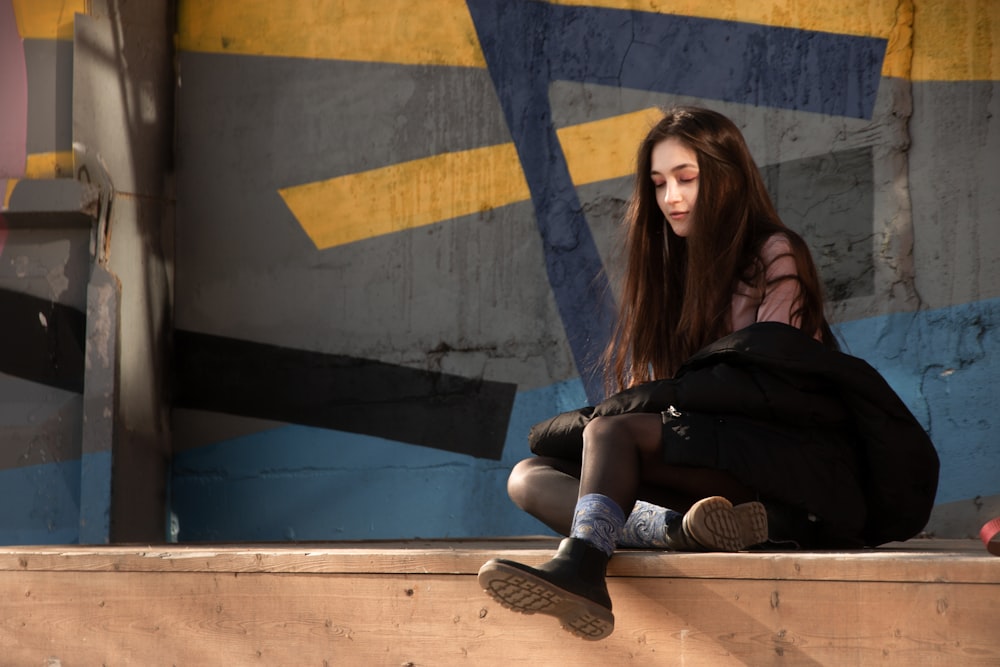 woman with black jacket sitting on concrete pavement