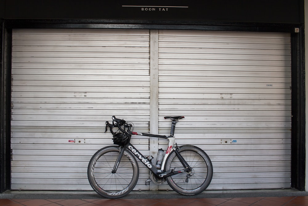 black and gray road bike leaning on roll-top door