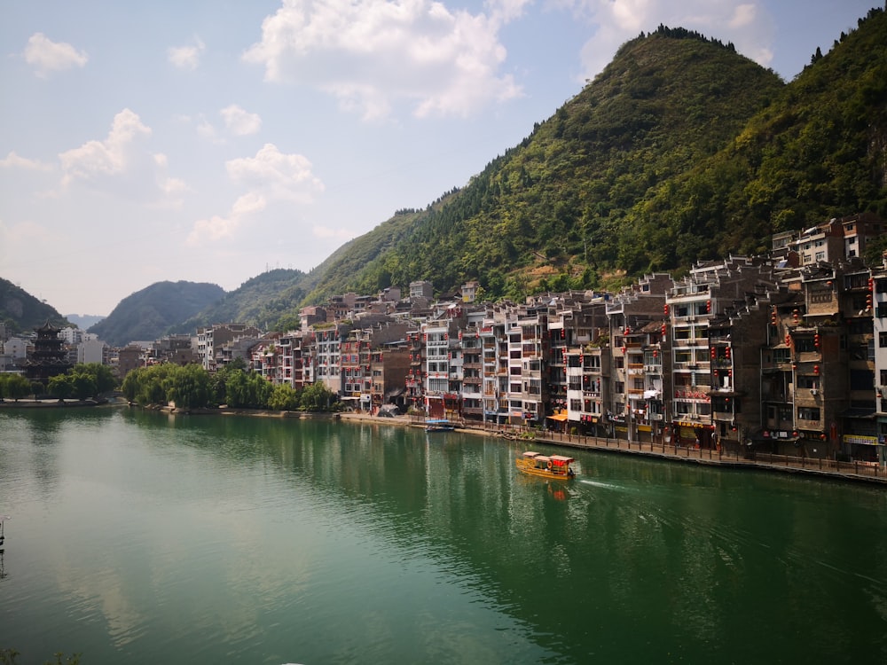 yellow and red boat on body of water viewing houses and building under white and blue skies during daytime