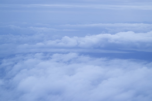 A vast expanse of clouds stretching across the sky, with layers of fluffy white clouds interspersed with soft blue hues. The cloud formations create a serene and peaceful atmosphere, providing a bird's-eye view from above.