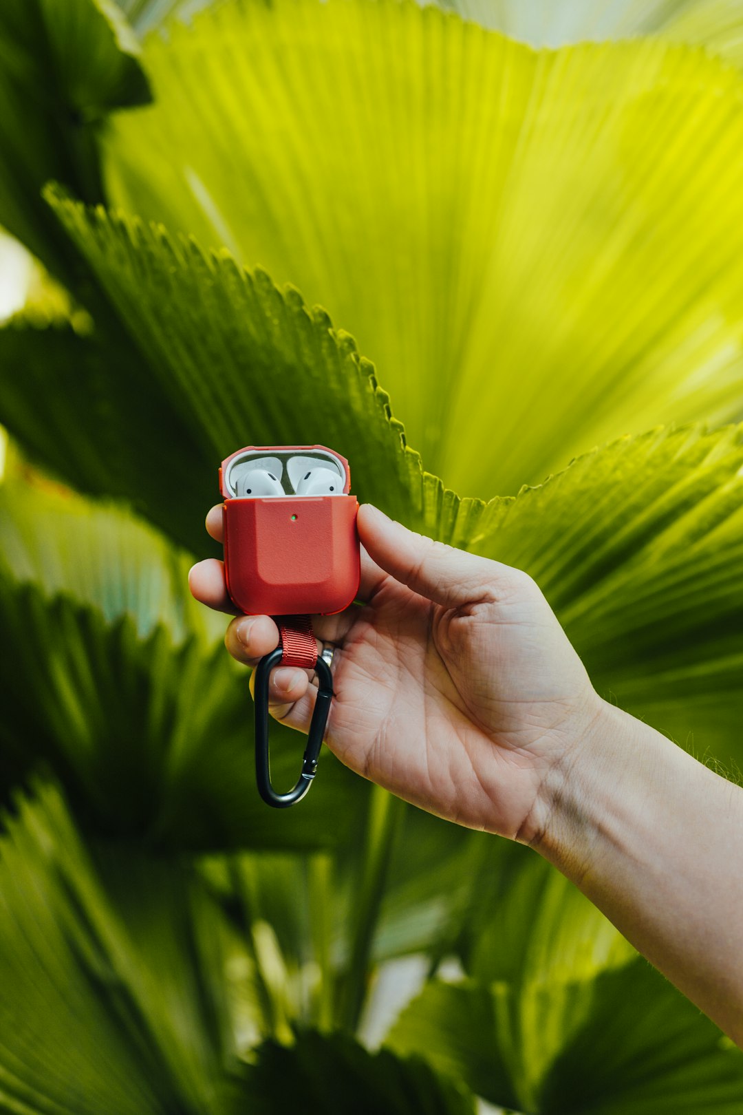 person holding red wireless earphones charging case