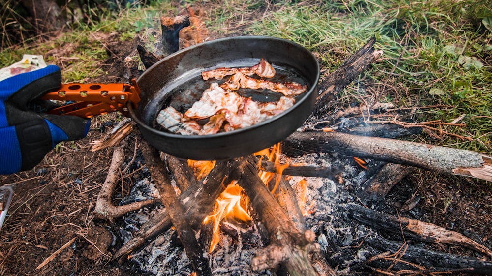 person holding wok with meat on to the fire