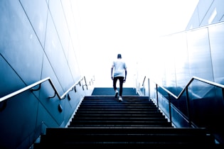 man wearing white crew-neck shirt and black pants walking upstairs