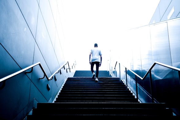 man wearing white crew-neck shirt and black pants walking upstairs