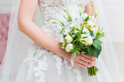 Bridal bouquet of delicate white and blush artificial flowers held by a bride.