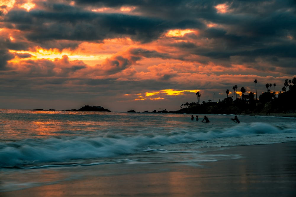 silhouette of people playing on seashore during sunset