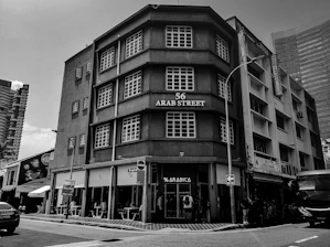 Historic black-and-white photo of Aboobacker Haji founding Chekkuppa Traders in 1955, blending into a modern image of the current headquarters in Malappuram.