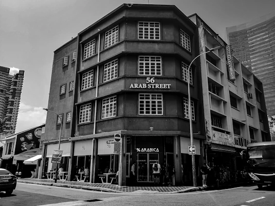 Historic black-and-white photo of Aboobacker Haji founding Chekkuppa Traders in 1955, blending into a modern image of the current headquarters in Malappuram.