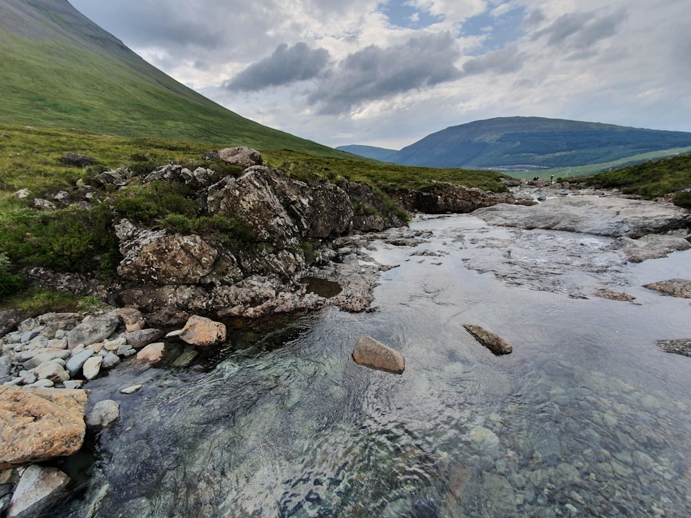 body of water near mountain under cloudy sky