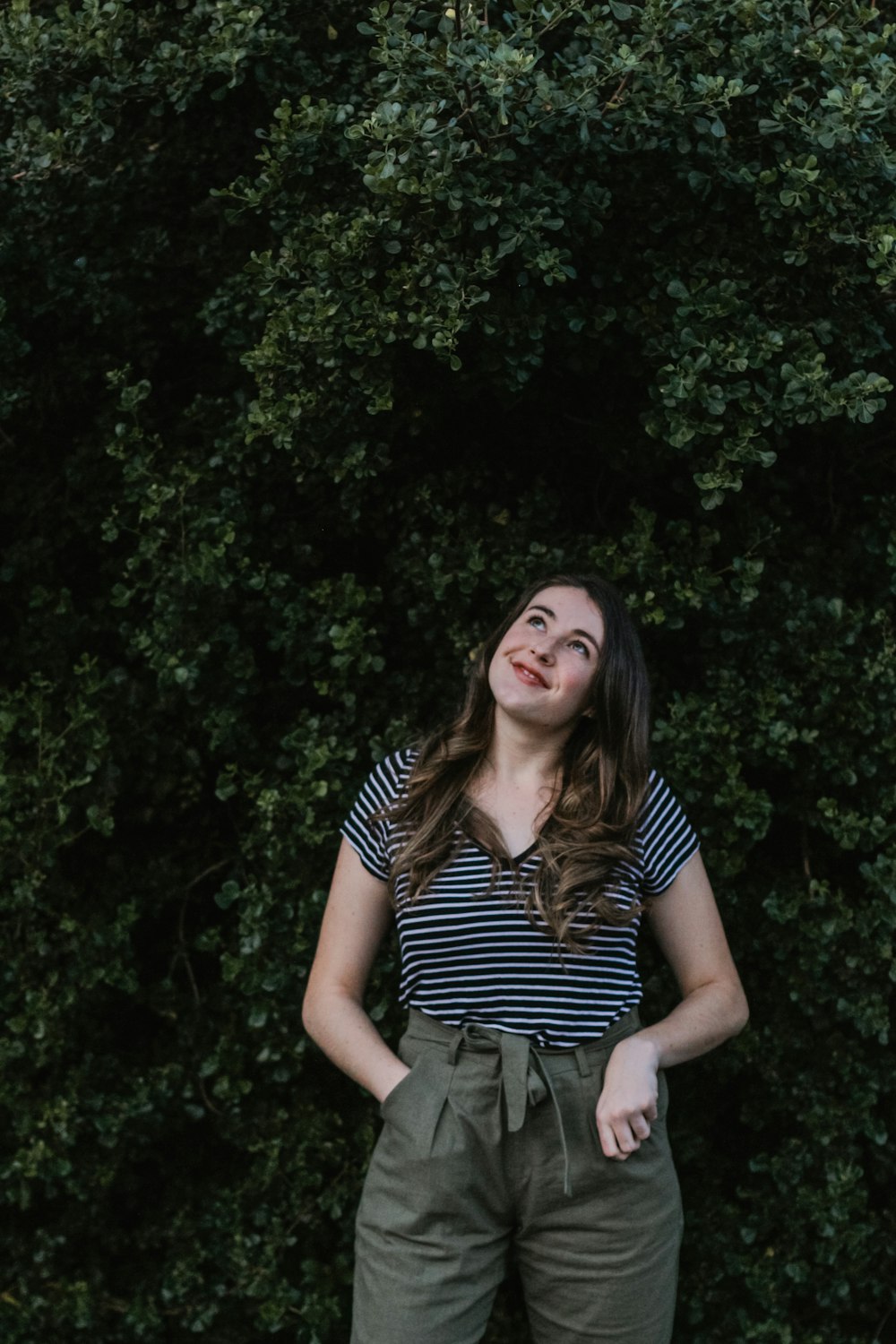 woman wearing black and white striped V-neck t-shirt looking up while standing near green leaf plants