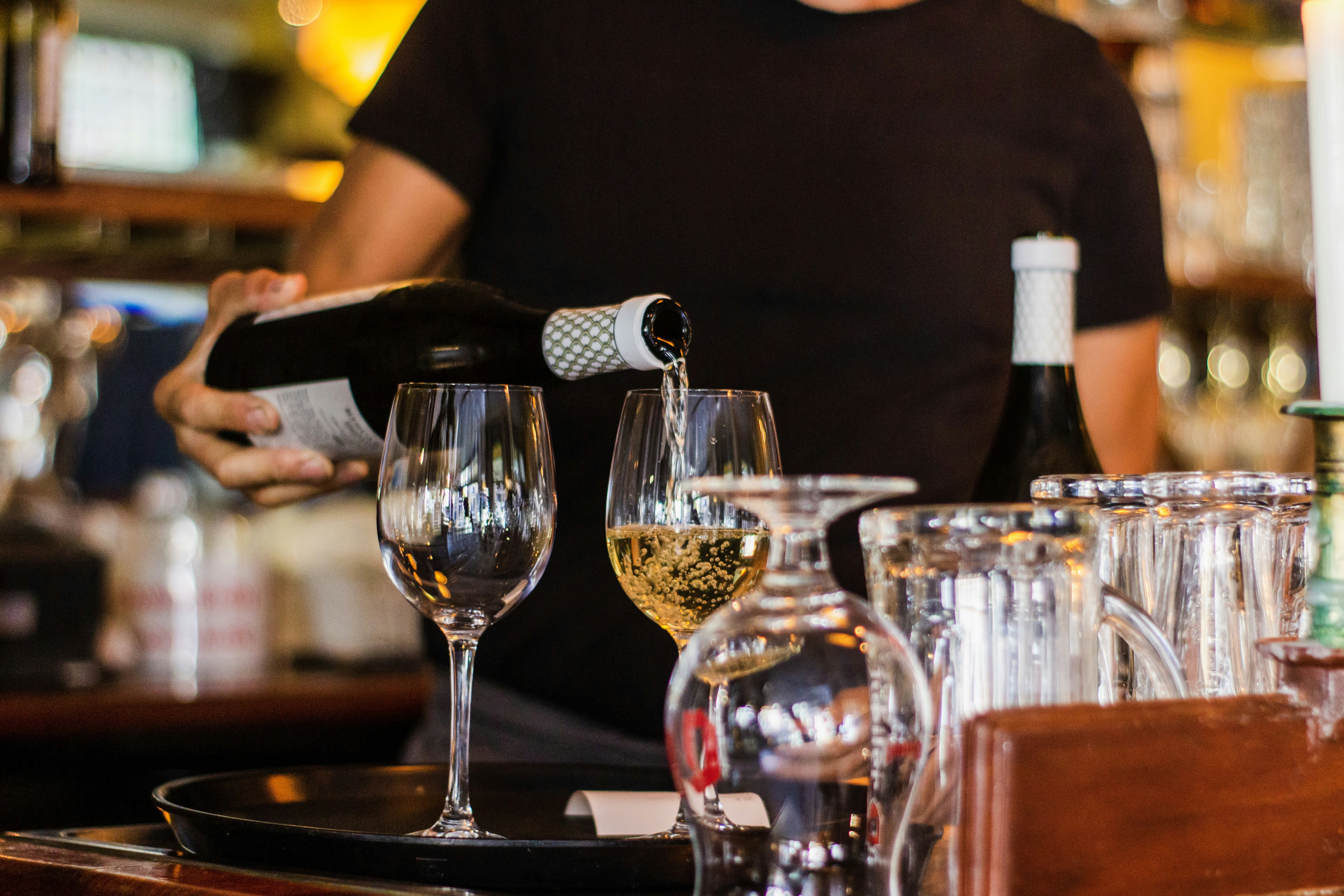 Bartender pouring wine into a glasses that are on a tray.