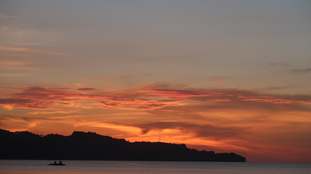 silhouette of mountain and boat at sea during golden hour