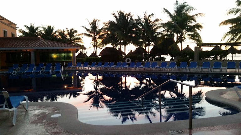 Outdoor pool area at sunset with loungers and palm trees.