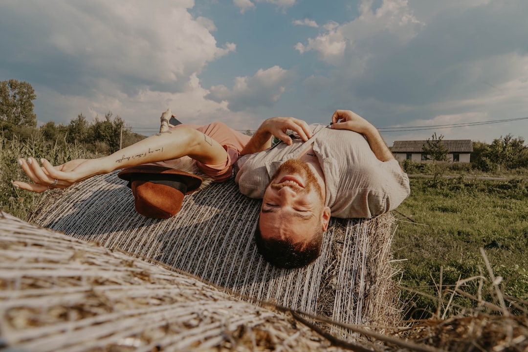 man lying on rolled hay bale along with a woman at daytime