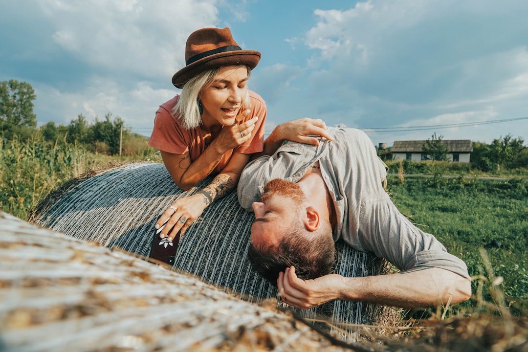 woman lying on hay bale along with woman in fedora hat at daytime
