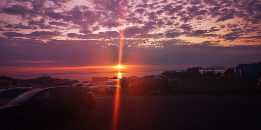 Sunset over the Grand River with tents and RVs nestled among lush trees at Maitland Shore campground.