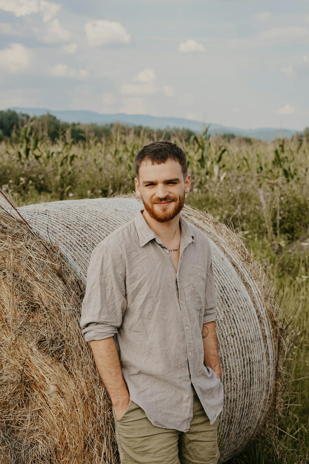smiling man in brown sports shirt leaning on rolled hay bale at daytime