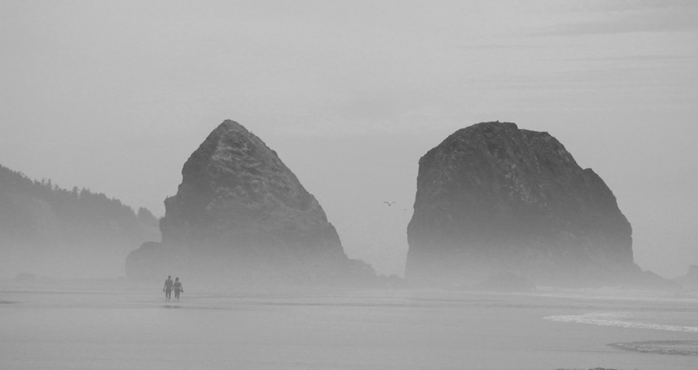 silhouette of two person walking on seashore during foggy weather