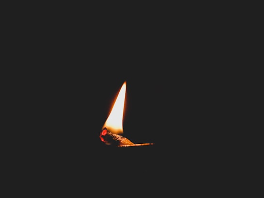 A single matchstick with a small, bright flame against a dark background, creating a stark contrast between light and darkness.