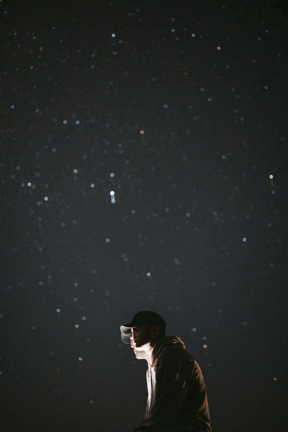 a man sitting on top of a wooden bench under a night sky filled with stars