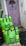 Two green Amazon Fresh delivery bags are placed on the ground in front of a uniquely painted purple door with decorative elements such as a crown and wings. The bags display various grocery items listed on them in white text. The surrounding area includes orange crates and a black mat, with the bags leaning against a wall.