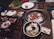 A variety of dishes are arranged on a table around an active grill. Fresh cuts of meat are cooking on the grill. There are also plates of raw and cooked foods including salad, sushi, and a vegetable platter. Small dishes of sauces are placed around the table.