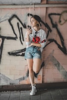 A young person rocking a rose gold-accented hoodie, leaning against a graffiti wall on a sunny day.