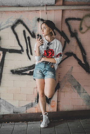 A young person rocking a rose gold-accented hoodie, leaning against a graffiti wall on a sunny day.