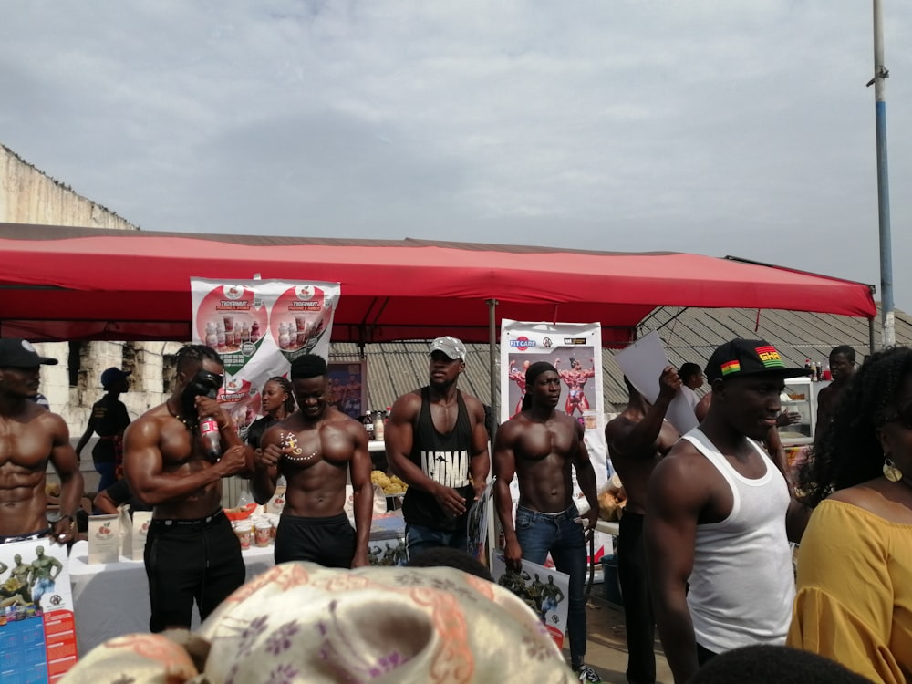 topless men standing near red gazebo during daytime