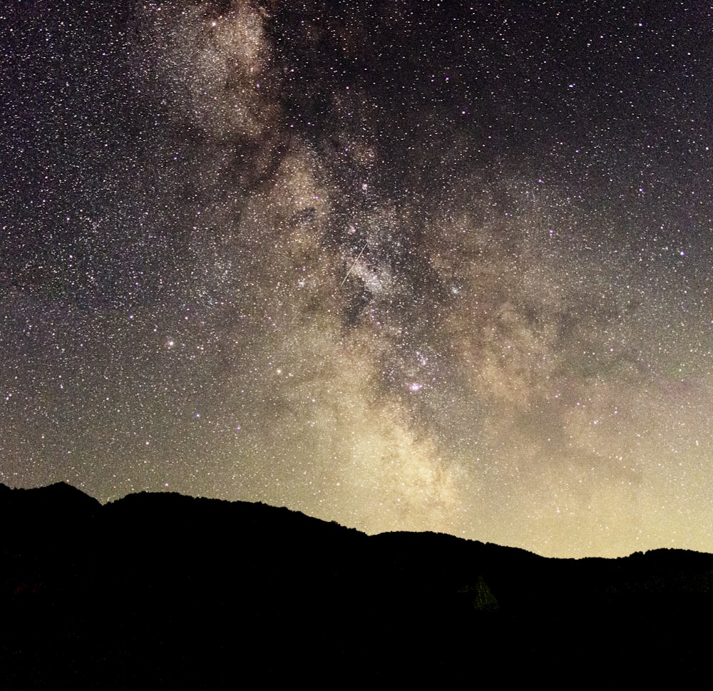 silhouette of mountain showing stars during night time