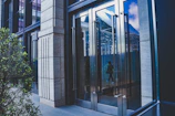 An elegant glass door entrance reflecting a sunny office building.