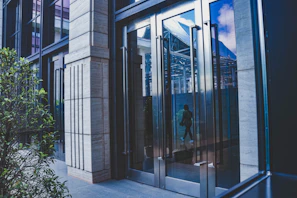 An elegant glass door entrance reflecting a sunny office building.